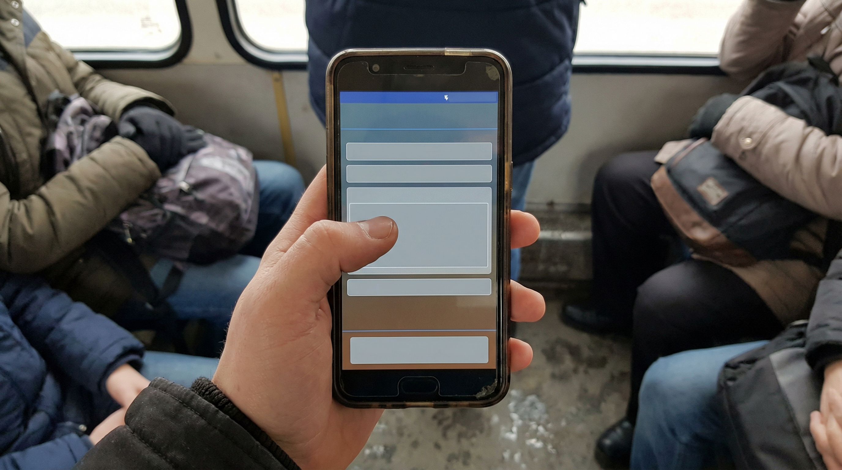 Overhead shot of a person using a slightly scuffed Android phone with one hand on a crowded bus, fil